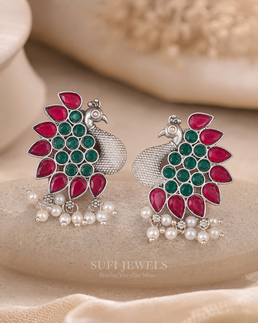 The Peacock Found Wings silver-look peacock stud earrings with red and green stones.
