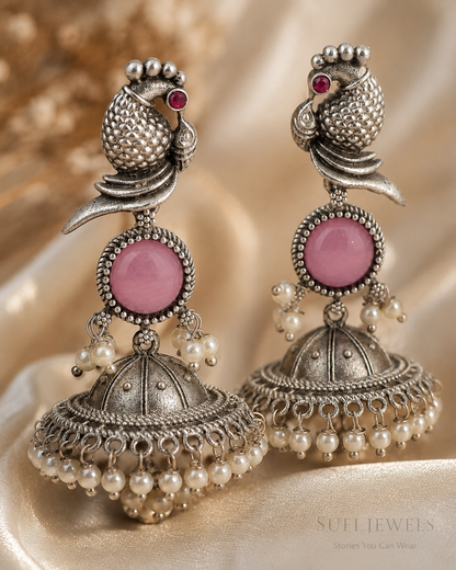 The Bird Carried Bells silver-look jhumka earrings with a sculpted bird motif, pink centre stone and white pearl detailing.